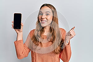 Young blonde woman holding smartphone showing screen screaming proud, celebrating victory and success very excited with raised arm