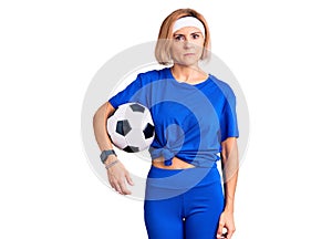 Young blonde woman holding soccer ball thinking attitude and sober expression looking self confident