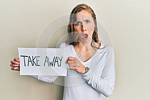 Young blonde woman holding take away food in shock face, looking skeptical and sarcastic, surprised with open mouth