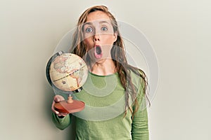 Young blonde woman holding vintage world ball scared and amazed with open mouth for surprise, disbelief face