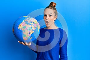 Young blonde woman holding world ball scared and amazed with open mouth for surprise, disbelief face