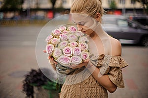 Young blonde woman holds bouquet of roses and sniffs it.