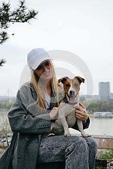 Young blonde woman hugs a dog in a spring park. Female owner with a Jack Russell terrier puppy on a walk, a close-up