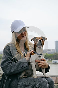 Young blonde woman hugs a dog in a spring park. Female owner with a Jack Russell terrier puppy on a walk, a close-up