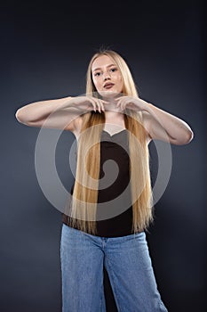 Young blonde woman in jeans and brown singlet on gray background