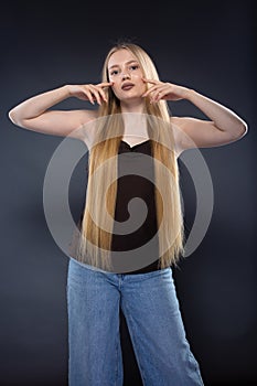 Young blonde woman in jeans and brown singlet on gray background