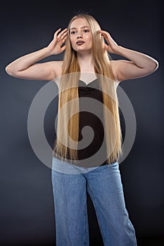 Young blonde woman in jeans and brown singlet on gray background