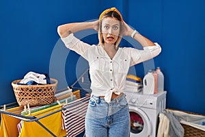 Young blonde woman at laundry room crazy and scared with hands on head, afraid and surprised of shock with open mouth