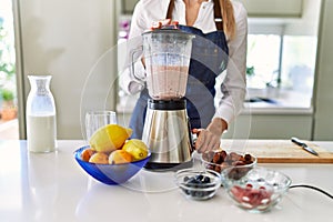 Young blonde woman liquefying smoothie using bender at kitchen