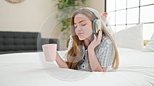 Young blonde woman listening to music drinking coffee at bedroom