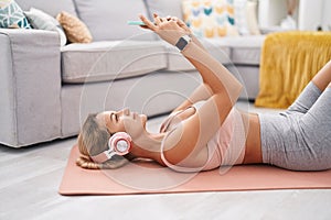 Young blonde woman listening to music lying on floor at home