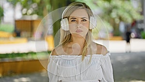 Young blonde woman listening to music with serious face at park