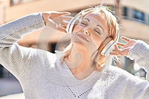 Young blonde woman listening to music at street