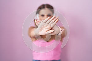 Young blonde woman listening to music using headphones rejection expression crossing arms and palms doing negative sign, angry