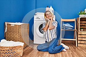 Young blonde woman listening to music waiting for washing machine at laundry room