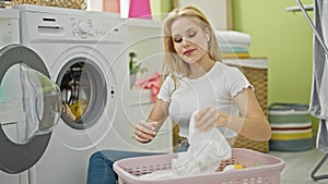 Young blonde woman listening to music washing clothes smiling at laundry room