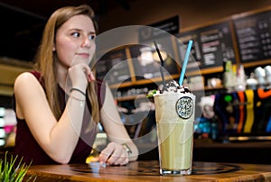 Young blonde woman in local cafe at wooden table drink frappe wi photo