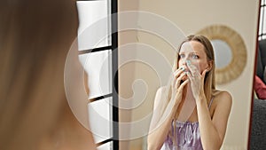 Young blonde woman looking face on mirror with upset expression at street