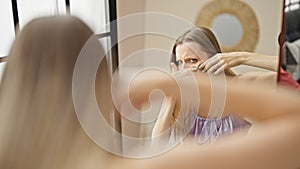 Young blonde woman looking on mirror popping pimples on face at street