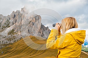 Young blonde woman looks in binoculars to high mountain pass in the Dolomites the Giau Pass