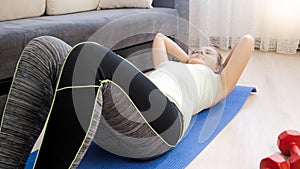 Young blonde woman lying on fitness mat at home and doing sit ups