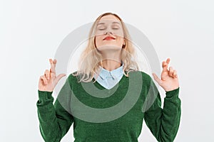 Young blonde woman makes wish with crossed fingers, wishing to achieve goal, praying with closed eyes, having hope for better
