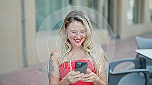 Young blonde woman making selfie by the smartphone sitting on table smiling at coffee shop terrace