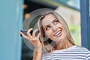 Young blonde woman miling confident listening audio message by the smartphone at street