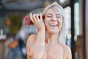 Young blonde woman miling confident listening audio message by the smartphone at street