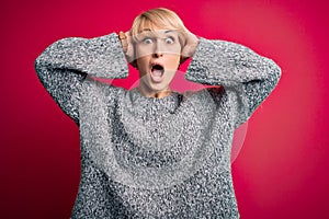 Young blonde woman with modern short hair wearing casual sweater over pink background Crazy and scared with hands on head, afraid