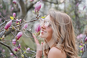 Young blonde woman near blossoming magnolia flowers tree in spring park on sunny day. Magnolia trees. Beautiful happy