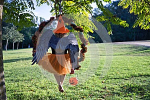 A young blonde woman in an orange hat and skirt with a pumpkin in her hand and with angel wings sitting on her back in an aerial