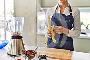 Young blonde woman peeling banana at kitchen