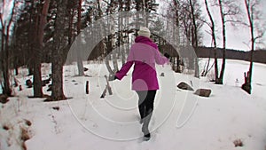 Young blonde woman in pink coat running in winter forest