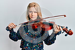 Young blonde woman playing violin skeptic and nervous, frowning upset because of problem