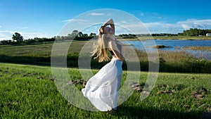 young blonde woman posing against the wind in landscape with peaceful face during sunset skirt & hair blown by the wind