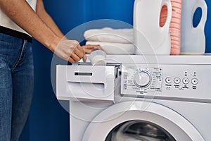 Young blonde woman pouring detergent on washing machine at laundry room