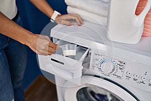 Young blonde woman pouring detergent on washing machine at laundry room