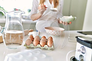 Young blonde woman pouring flour on bowl at kitchen