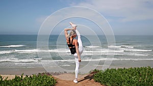 Young blonde woman practicing yoga pose near the ocean.