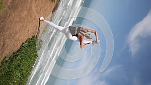 Young blonde woman practicing yoga pose near the ocean.