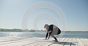 Young Blonde Woman practicing yoga on the wooden berth at lake. Single sport healthy training on nature at sunny weather