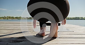 Young Blonde Woman practicing yoga on the wooden berth at lake. Single sport healthy training on nature at sunny weather