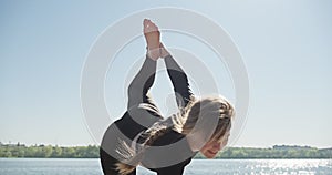 Young Blonde Woman practicing yoga on the wooden berth at lake. Single sport healthy training on nature at sunny weather