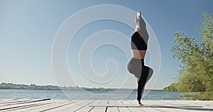 Young Blonde Woman practicing yoga on the wooden berth at lake. Single sport healthy training on nature at sunny weather