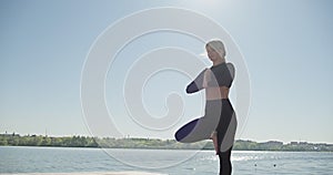 Young Blonde Woman practicing yoga on the wooden berth at lake. Single sport healthy training on nature at sunny weather