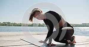 Young Blonde Woman practicing yoga on the wooden berth at lake. Single sport healthy training on nature at sunny weather