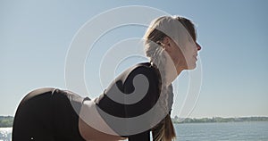 Young Blonde Woman practicing yoga on the wooden berth at lake. Single sport healthy training on nature at sunny weather