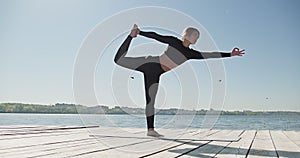 Young Blonde Woman practicing yoga on the wooden berth at lake. Single sport healthy training on nature at sunny weather