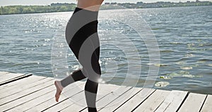 Young Blonde Woman practicing yoga on the wooden berth at lake. Single sport healthy training on nature at sunny weather